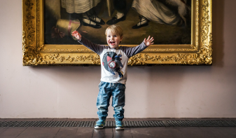 Child with hands up in front of a painting